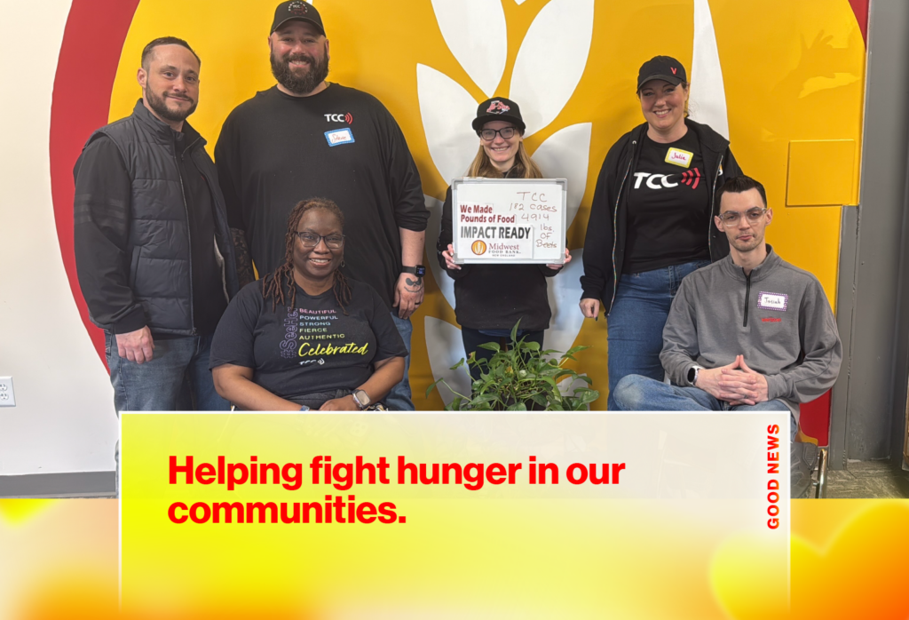 Six volunteers pose for a group photo in front of a bright mural, one holding a sign about food donations for a drive event