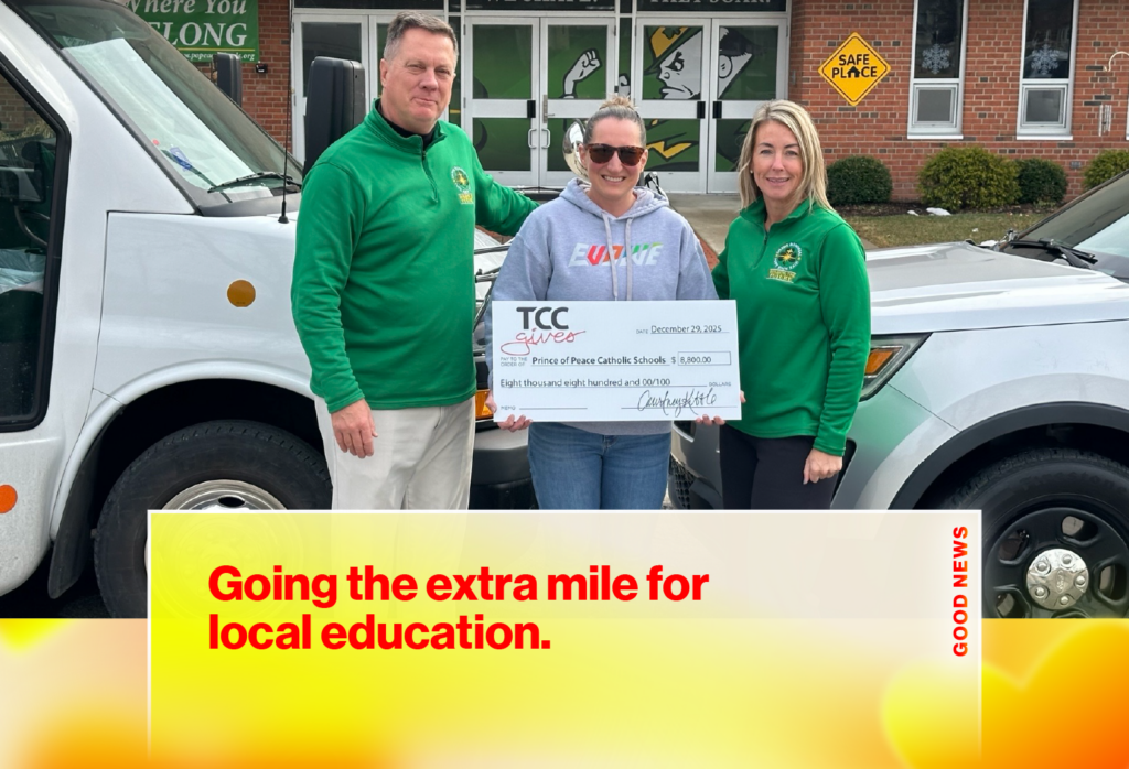 Three people stand in front of a school entrance, holding a large donation check from TCC Gives to Prince of Peace Catholic Schools dated December 29, 2025.