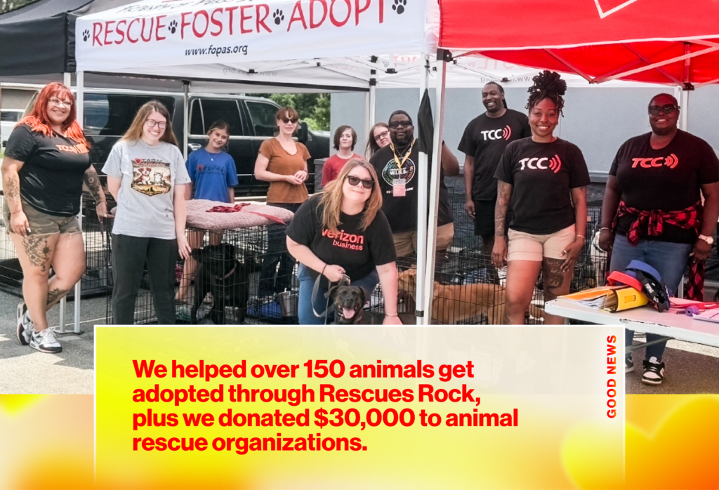Group of volunteers posing at a Rescue Foster Adopt booth outdoors, with dogs in cages nearby, smiling for the camera.