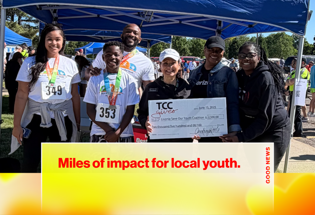 Group of volunteers at an outdoor fundraiser posing with a large ceremonial check for youth organization turnout under blue tents.