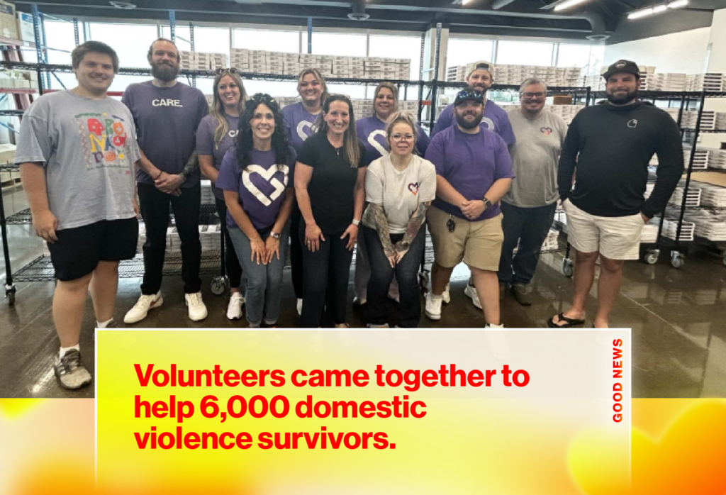 Group of volunteers in a warehouse posing behind a banner that reads, 'Volunteers came together to help 6,000 domestic violence survivors'.